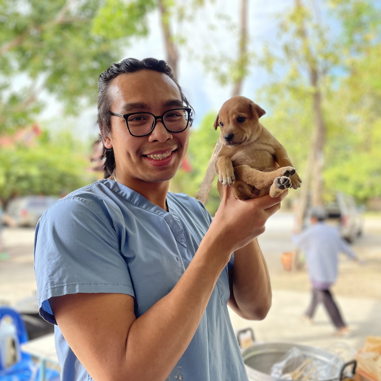A FARVets clinician smiling while holding a small puppy at an outdoor clinic